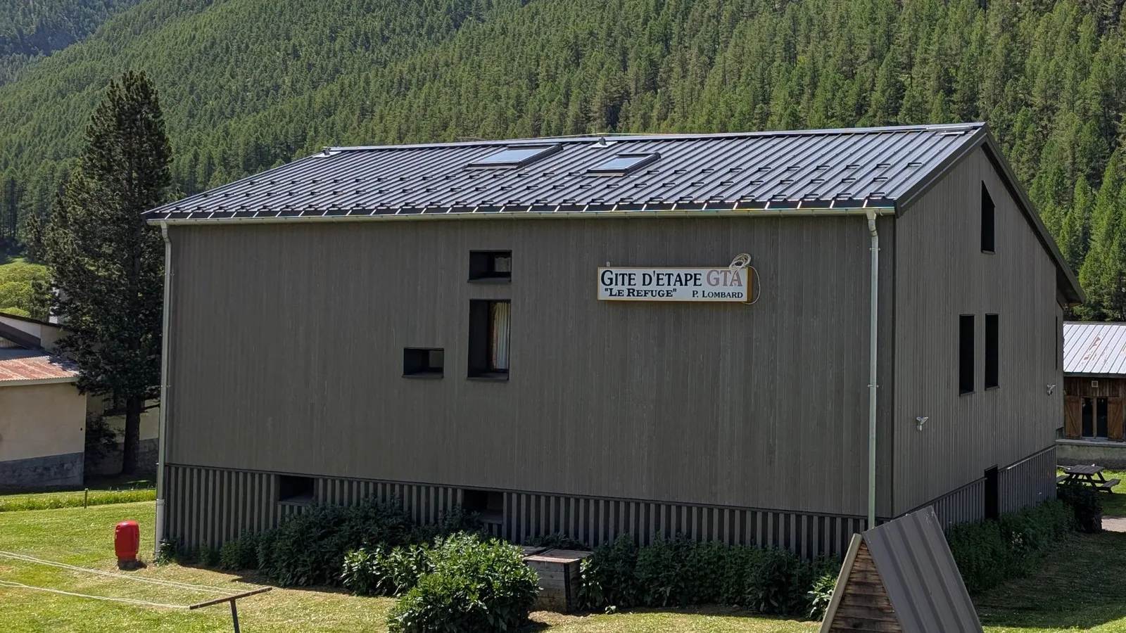 Le gîte d'étape Le Refuge à Larche, bâtiment de bois devant les mélézins