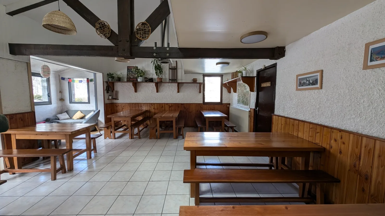 La salle commune : grandes tablées en bois, poutres et coin salon