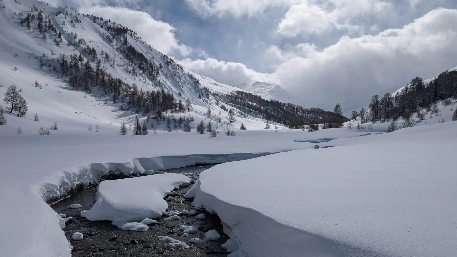 La vallée enneigée en hiver, le torrent serpentant entre les congères